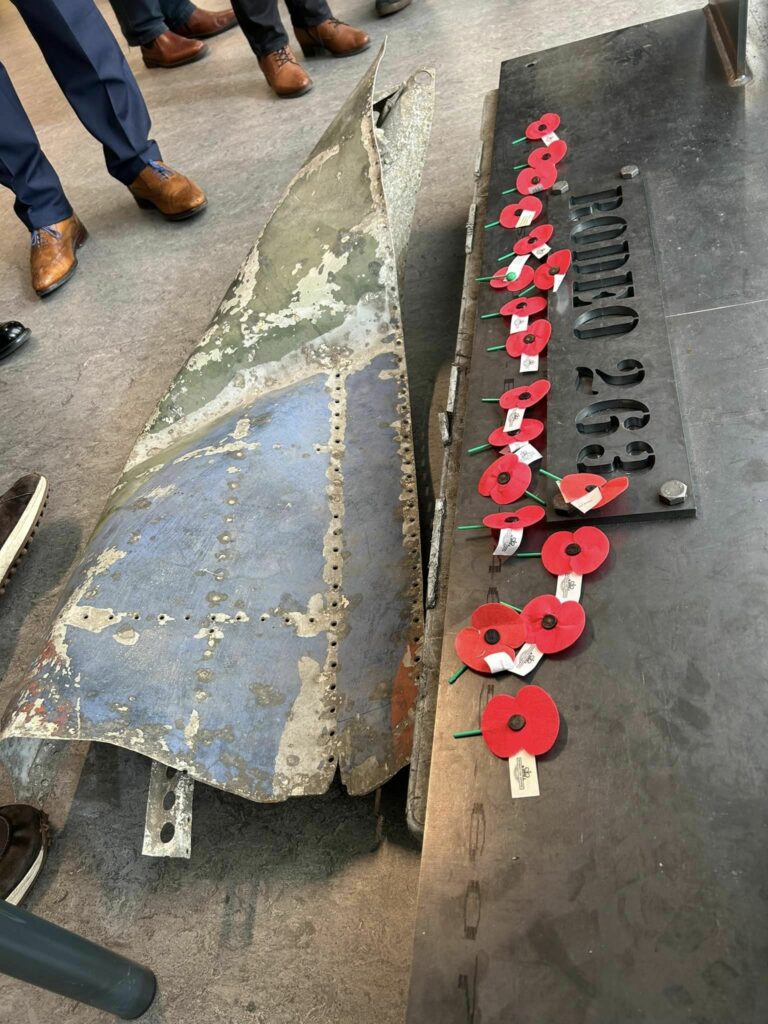 A piece of one of the Spitfire's wings was displayed with the memorial during the unveiling, and those assembled placed poppies on the memorial in remembrance of Baker and Thomson. [Photo by Lieven Vandecaveye]