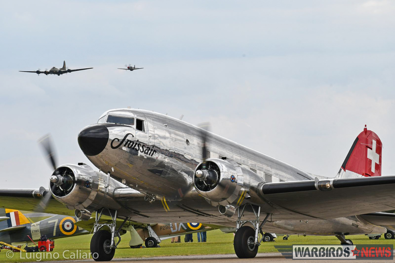 A fabulously maintained Swiss-based DC-3 taxies past a row of Hawker Hurricanes while B-17G 'Sally-B' flies overhead in company of a 'Little Friend'. (photo by Luigino Caliaro)