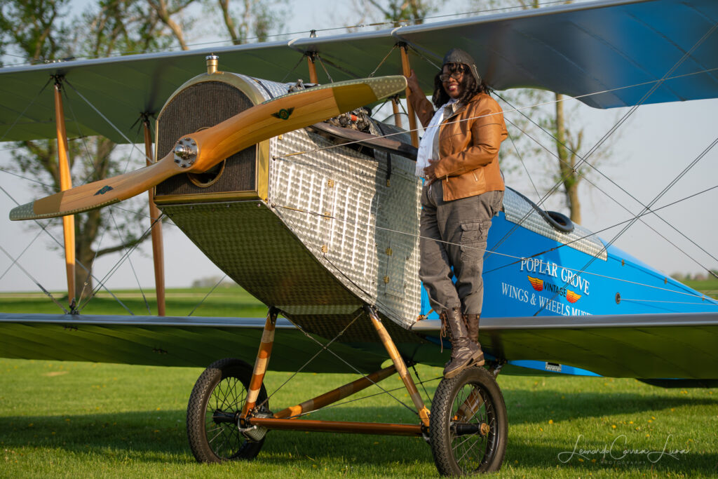 Gigi Coleman standing on the wheel of a Curtiss JN-4 "Jenny", built by Chapter 1414 of the Experimental Aircraft Association and the Vintage Wings and Wheels Museum, at Poplar Grove, Illinois in 2014. [Photo by Leonardo Correa Luna]
