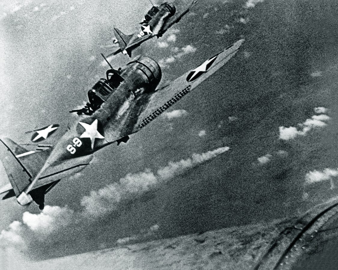U.S. Navy Douglas SBD-3 "Dauntless" dive bombers from scouting squadron VS-8 from the aircraft carrier USS Hornet (CV-8) approaching the burning Japanese heavy cruiser Mikuma to make the third set of attacks on her, during the Battle of Midway, 6 June 1942. Mikuma had been hit earlier by strikes from Hornet and USS Enterprise (CV-6), leaving her dead in the water and fatally damaged. Note bombs hung beneath the SBDs. U.S. Navy photo
