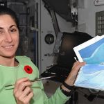 Nicole Stott in the International Space Station holding two of the watercolor paintings she created in space. NASA Nicole Stott