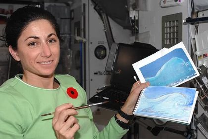 Nicole Stott in the International Space Station holding two of the watercolor paintings she created in space. NASA Nicole Stott