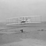 Orville Wright takes off in the first flight of the 1903 flyer as Wilbur Wright assists