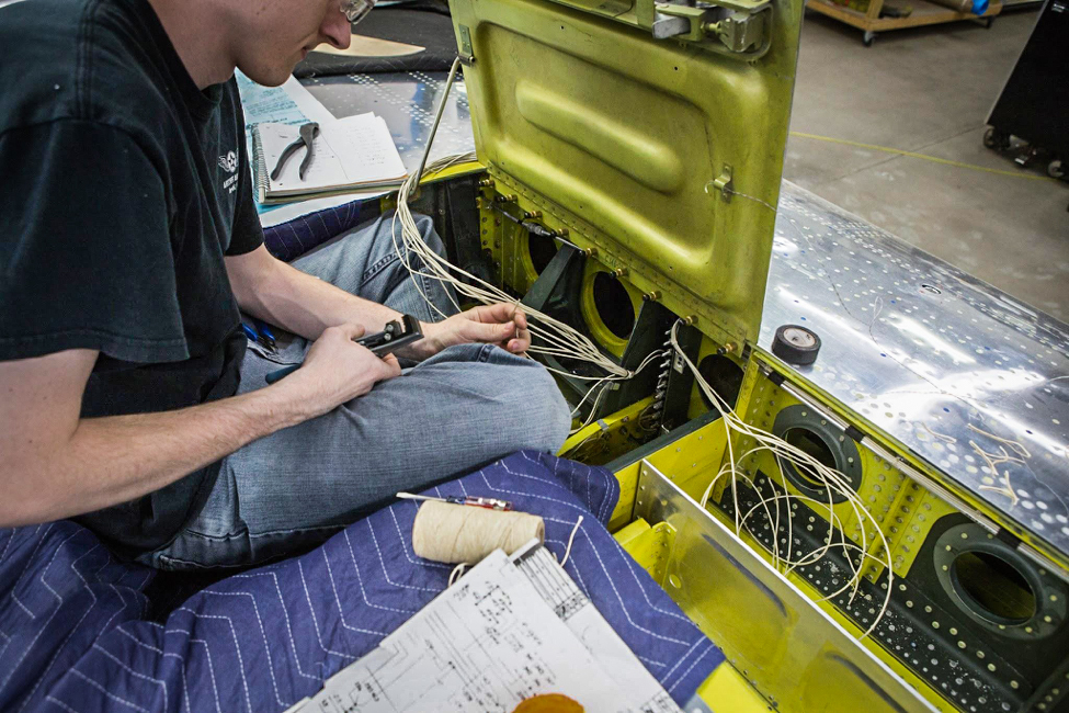 Aaron works to connect the various harnesses to the terminal strip visible ahead of his knee. (photo via AirCorps Aviation)