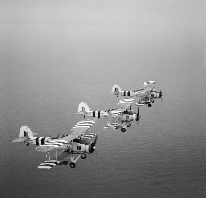 Rocket-armed Fairey Swordfish on a training flight from RNAS St Merryn in Cornwall, 1 August 1944. Three rocket projectile Fairey Swordfish during a training flight from St Merryn Royal Naval Air Station This operational squadron was commanded by Lieutenant Commander P Snow RN. Note the invasion stripes carried for the Normandy landings on the wings and fuselage of the aircraft.
