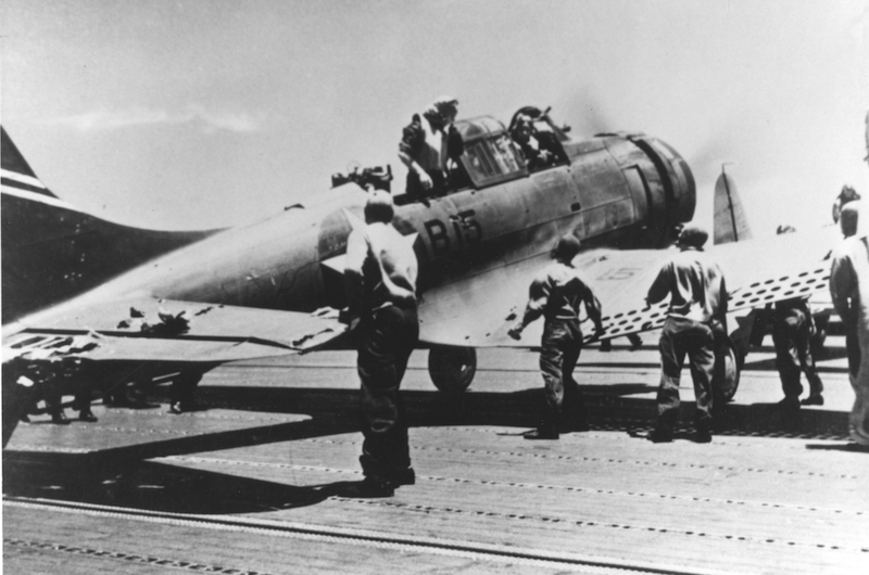 A U.S. Navy Douglas SBD-3 "Dauntless" scout bomber (BuNo 4542), of Bombing Squadron Six (VB-6) from USS Enterprise (CV-6), after landing on USS Yorktown (CV-5) at about 1140 hrs on 4 June 1942, during the Battle of Midway. This plane, damaged during the attack on the Japanese aircraft carrier Kaga that morning, landed on Yorktown as it was low on fuel. It was later lost with the carrier. Its crew, Ensign George H. Goldsmith, pilot, and Radioman 1st Class James W. Patterson, Jr., are still in the cockpit. Note damage to the horizontal tail.