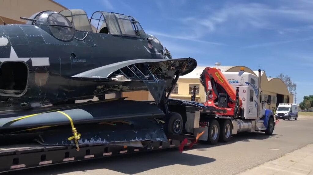 Strapped to a flatbed trailer towed by Polar King International TBM Avenger 91188 arrives at the Castle Air Museum restoration hangar Castle Air Museum