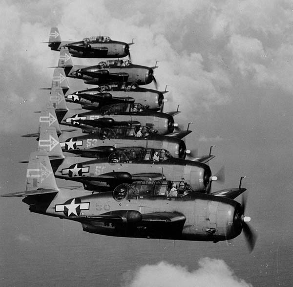 Seven Grumman TBM-3D Avenger bombers of night torpedo squadron VT(N)-90 flying in formation in January 1945. The squadron was part of Night Air Group 90 on the carrier USS Enterprise (CV-6). Note radar pods in right-side wings, and the distinctive tail insignia. (Image via Wikipedia)